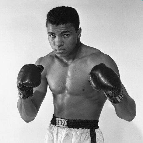 A black-and-white photo of an unidentified male boxer in a fighting stance, wearing boxing gloves and shorts.