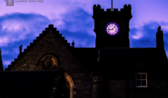 Lerwick Town Hall at dusk, with the clock tower illuminated against a purple and blue sky.