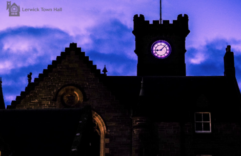 Lerwick Town Hall at dusk, with the clock tower illuminated against a purple and blue sky.