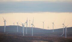 A distant view of numerous wind turbines on a barren landscape under an overcast sky.