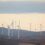 A distant view of numerous wind turbines on a barren landscape under an overcast sky.