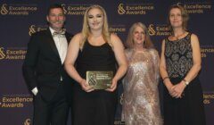 Four people stand in front of a Scotland Food & Drink Excellence Awards backdrop. One person holds a plaque that reads "Excellence Awards 2023". They are all dressed in formal attire and smiling.