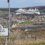 A road sign welcomes visitors to Lerwick, with a large cruise ship docked in the background and the town spread out along the coastline.