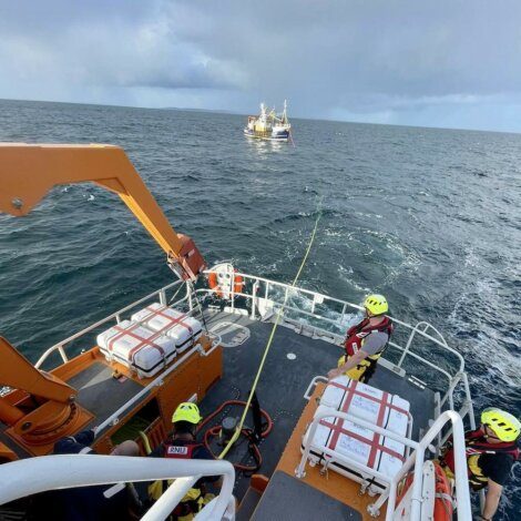 Rescue boat crew preparing for operation with fishing vessel in background at sea.