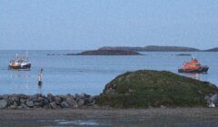 Two boats anchored near a coastline with a small islet in the background at dusk.