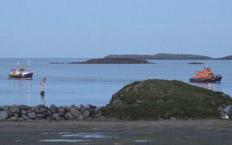 Two boats anchored near a coastline with a small islet in the background at dusk.