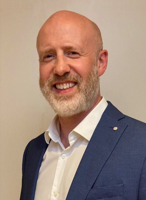 A smiling bald man wearing a suit and white shirt.