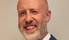 A smiling bald man with a beard wearing a suit jacket and white shirt.