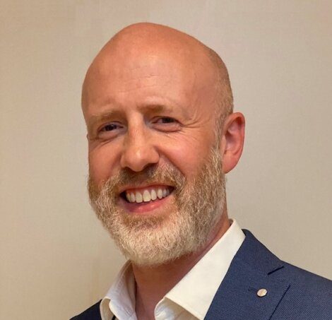 A smiling bald man with a beard wearing a suit jacket and white shirt.