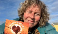 A person holding a 'world wild day' pamphlet smiles outdoors on a sunny day.