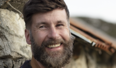 A smiling bearded man with a patterned sweater outdoors.