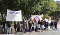 Group of individuals participating in a march with banners promoting recovery from addiction.