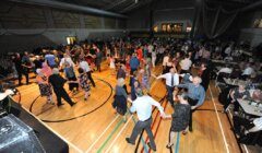 People dancing and socializing at an indoor event or gathering with tables set around the perimeter of the dance floor.