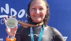 A smiling woman in a wetsuit proudly displaying her medal at a sporting event.