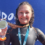 A smiling woman in a wetsuit proudly displaying her medal at a sporting event.