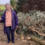 Elderly woman standing next to cut branches, holding a walking stick.