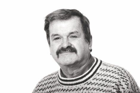 Black and white photo of a middle-aged man with a mustache, wearing a patterned sweater, looking at the camera with a neutral expression.