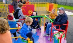 Children and adults enjoying a colorful, inclusive playground carousel designed for users of all abilities.