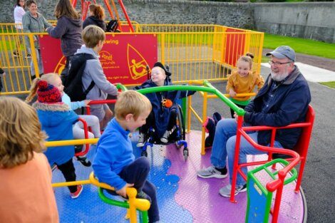 Children and adults enjoying a colorful, inclusive playground carousel designed for users of all abilities.