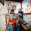 Woman in a ticket booth holding up a 'tall ship' brochure with a smile.