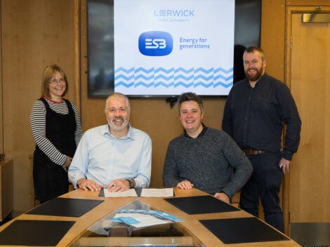 Four professionals posing for a photo in a conference room with a presentation screen displaying company logos in the background.