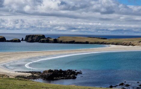 A serene coastal landscape featuring a sandy bay with clear blue waters, flanked by rocky outcrops under a partly cloudy sky.