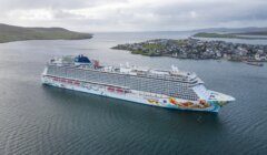 A large cruise ship near a coastal town with clear views of the landscape and water.