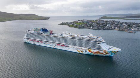 A large cruise ship near a coastal town with clear views of the landscape and water.