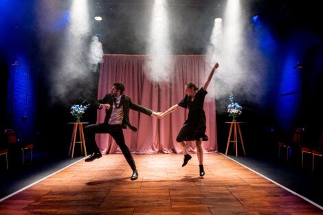 Two dancers performing on stage with theatrical lighting and smoke effects.