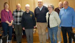 Group of seven adults standing in a room and smiling for a photo.