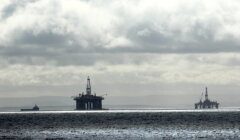 Offshore oil rigs and a supply vessel at sea under a cloudy sky.