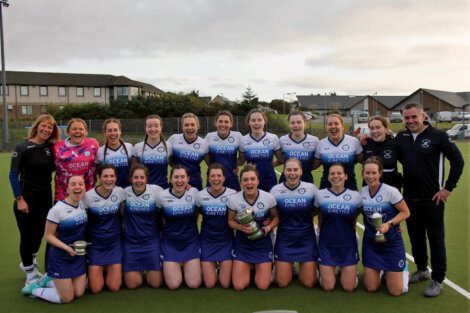 A group of field hockey players posing together on the pitch, smiling after a game or event.