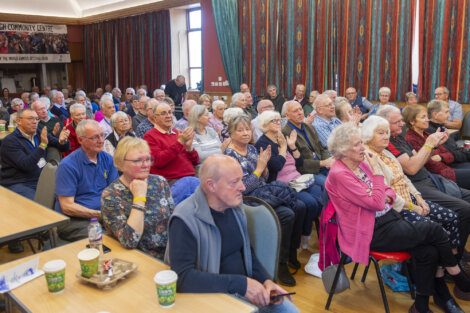 A group of senior adults attentively seated in a community center hall.