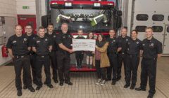 Firefighters posing with community members during a check presentation ceremony at the fire station.