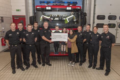 Firefighters posing with community members during a check presentation ceremony at the fire station.