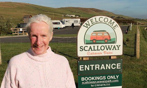 A smiling woman standing in front of a "welcome to scalloway caravan park" sign.