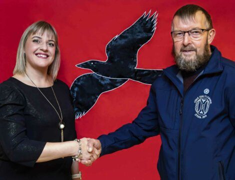 Two individuals shaking hands in front of a red background with a black bird silhouette.