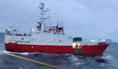 A red and white fishing boat named "antonio maria" at sea connected by a rope, with a dark sky above.