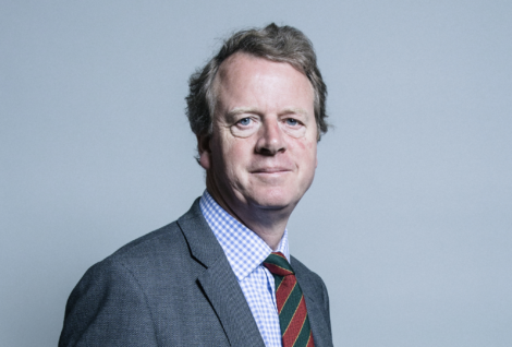 A middle-aged man with a slight smile wearing a suit, striped tie, and white shirt, posing for a portrait against a plain background.