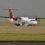 A turboprop passenger airplane parked on an airstrip with mountains in the background.