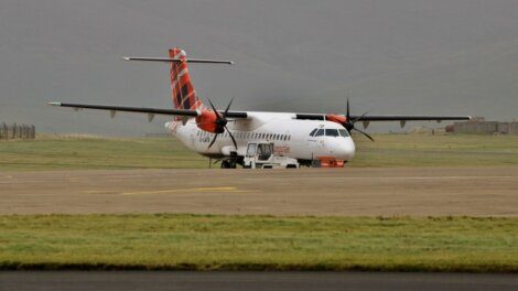 A turboprop passenger airplane parked on an airstrip with mountains in the background.