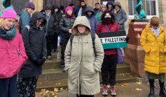 Group of people gathered for a demonstration, with one person in the foreground holding a "free palestine" sign.