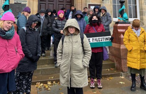 Group of people gathered for a demonstration, with one person in the foreground holding a "free palestine" sign.