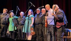 A group of musicians with various instruments standing on stage, smiling and taking a bow after a performance.