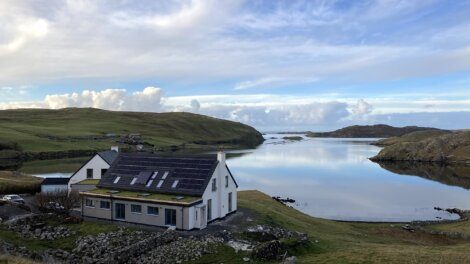 A house sits on top of a hill overlooking a body of water.