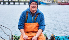 A man in overalls sitting on a boat.