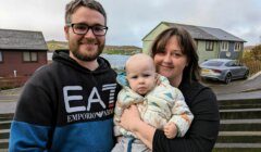 A man and woman holding a baby in front of a house.