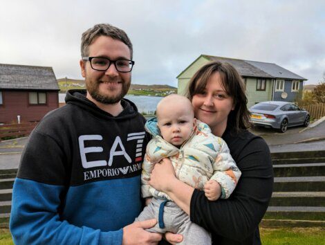 A man and woman holding a baby in front of a house.