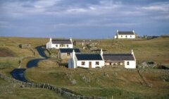 Rural landscape with winding road leading to white houses against a clear sky.