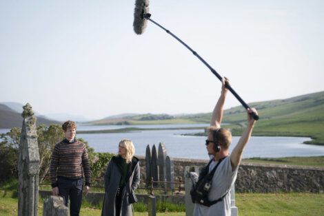 Two actors walking through a graveyard during a film shoot with a boom operator capturing audio.